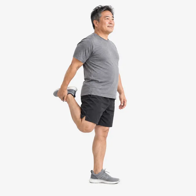 A smiling man doing a standing quad stretch