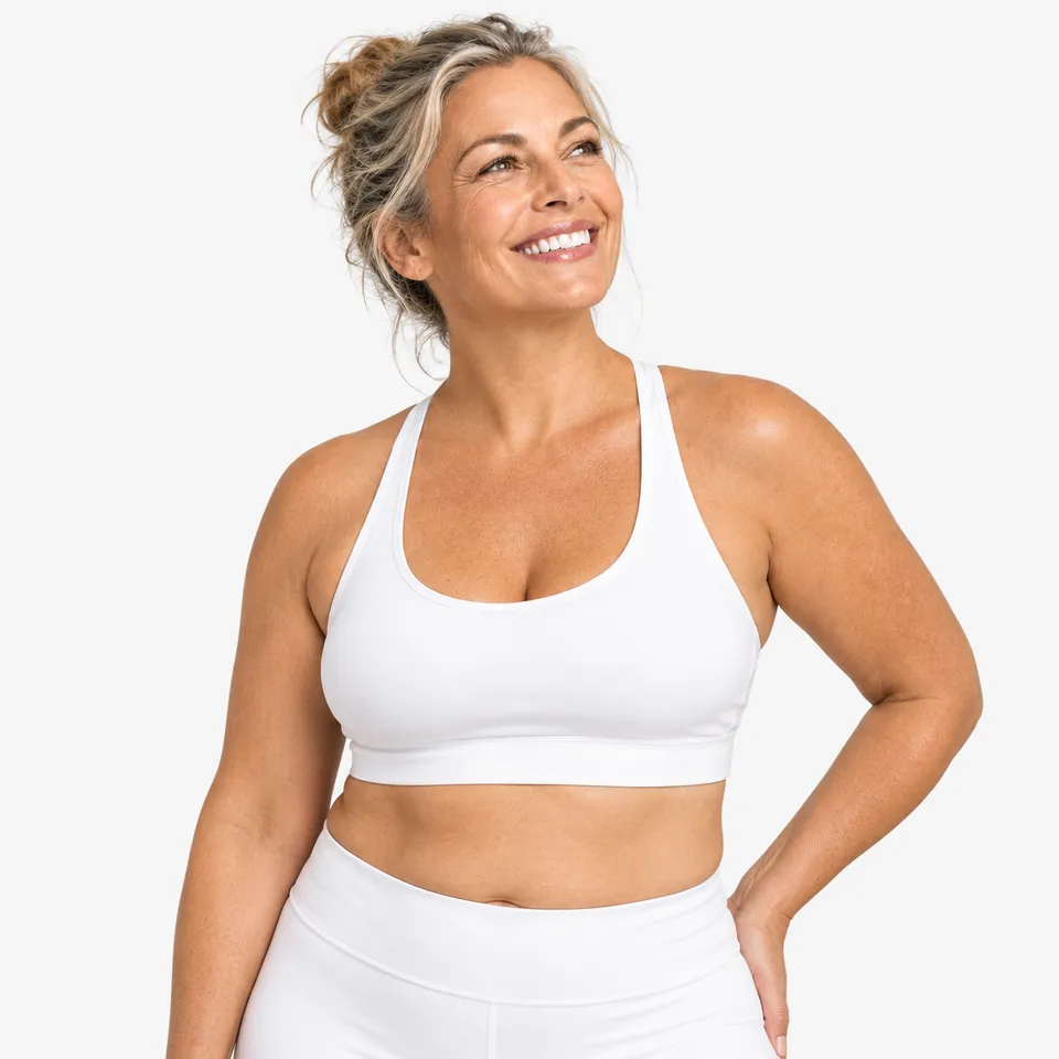 A smiling woman in a white sports top, one hand on her hip