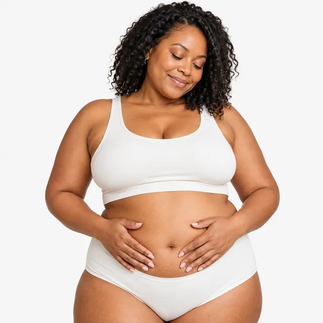 A smiling woman with curly hair resting her hands on her stomach