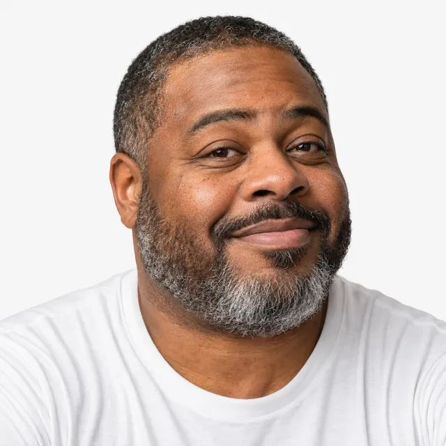 A smiling man with a gray beard in a white T-shirt