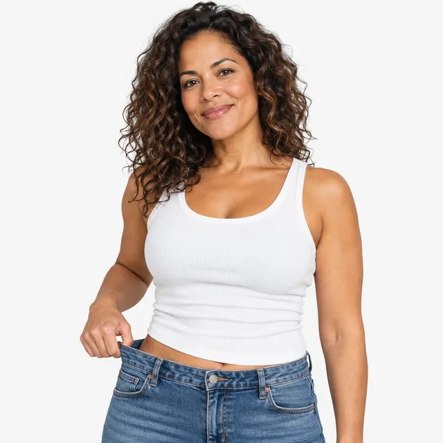 A smiling woman with curly hair in a white tank top and jeans