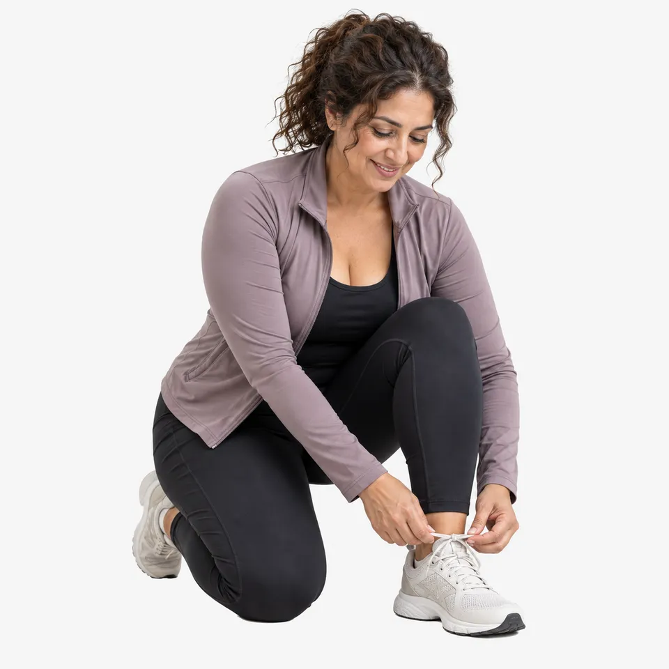 A smiling woman kneeling to tie her sneakers