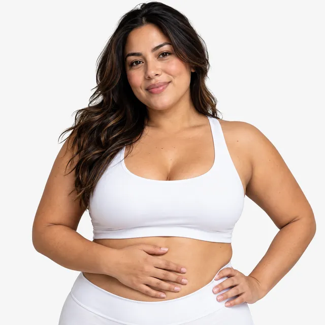 A smiling woman in white activewear with one hand on her stomach