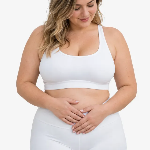 A woman in a white sports top with her hands on her stomach