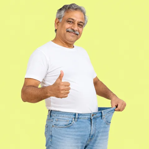 A smiling man with a gray moustache giving a thumbs up and holding out the loose waistband of his jeans
