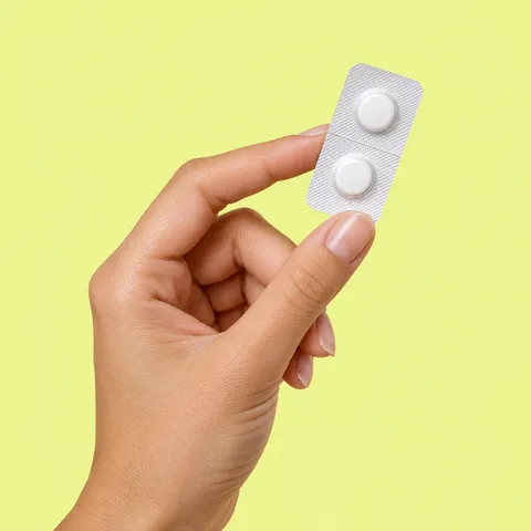 A hand holding a blister pack of two white tablets